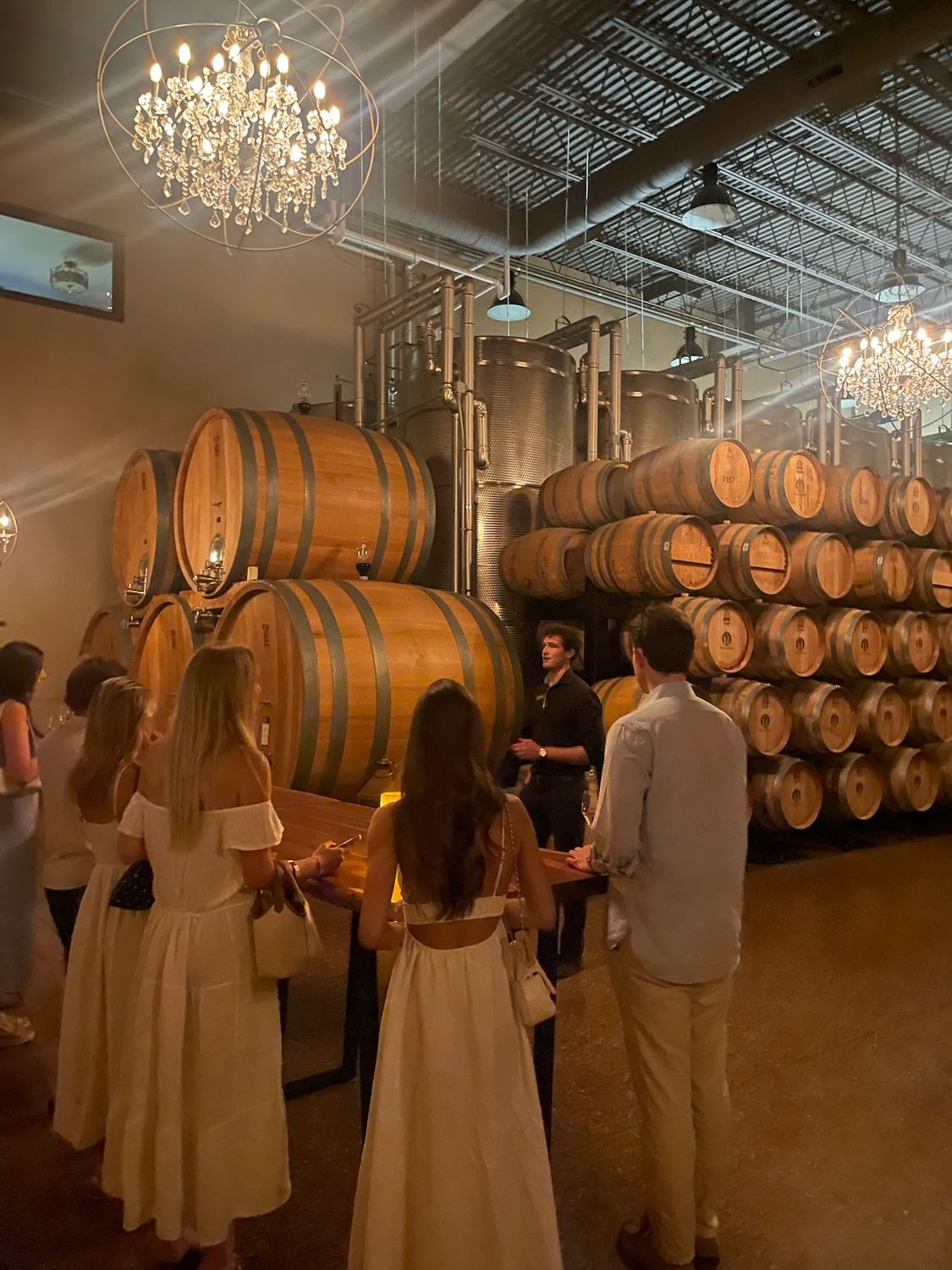 Members gathered among the barrels beneath a chandelier