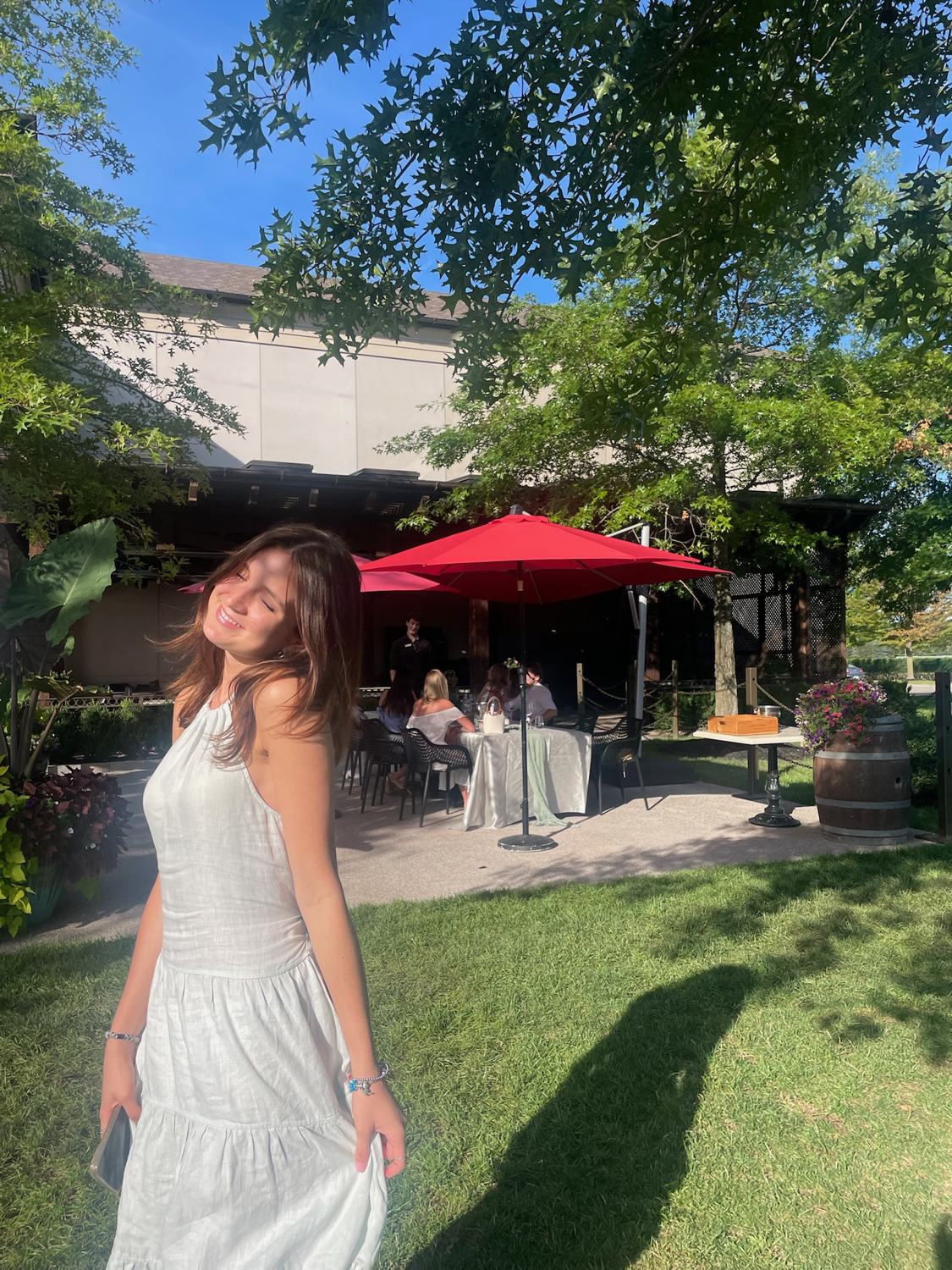 A member in a white dress on the winery lawn in the afternoon sun