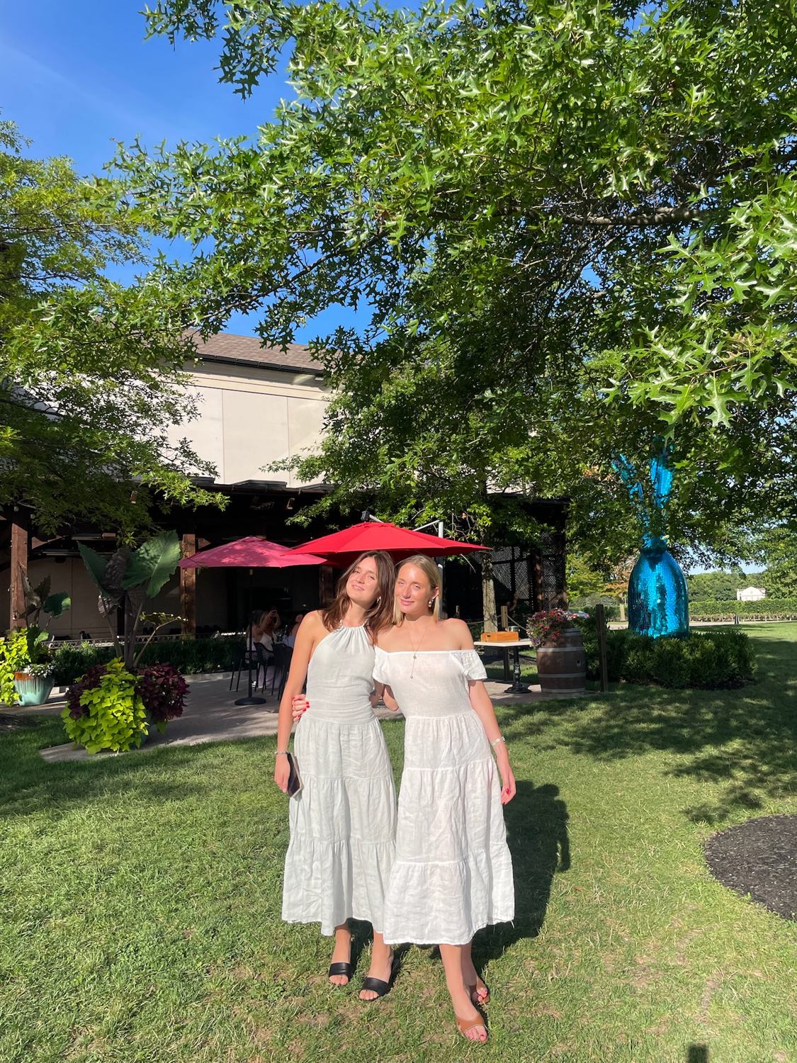 Two members in white dresses on the winery lawn