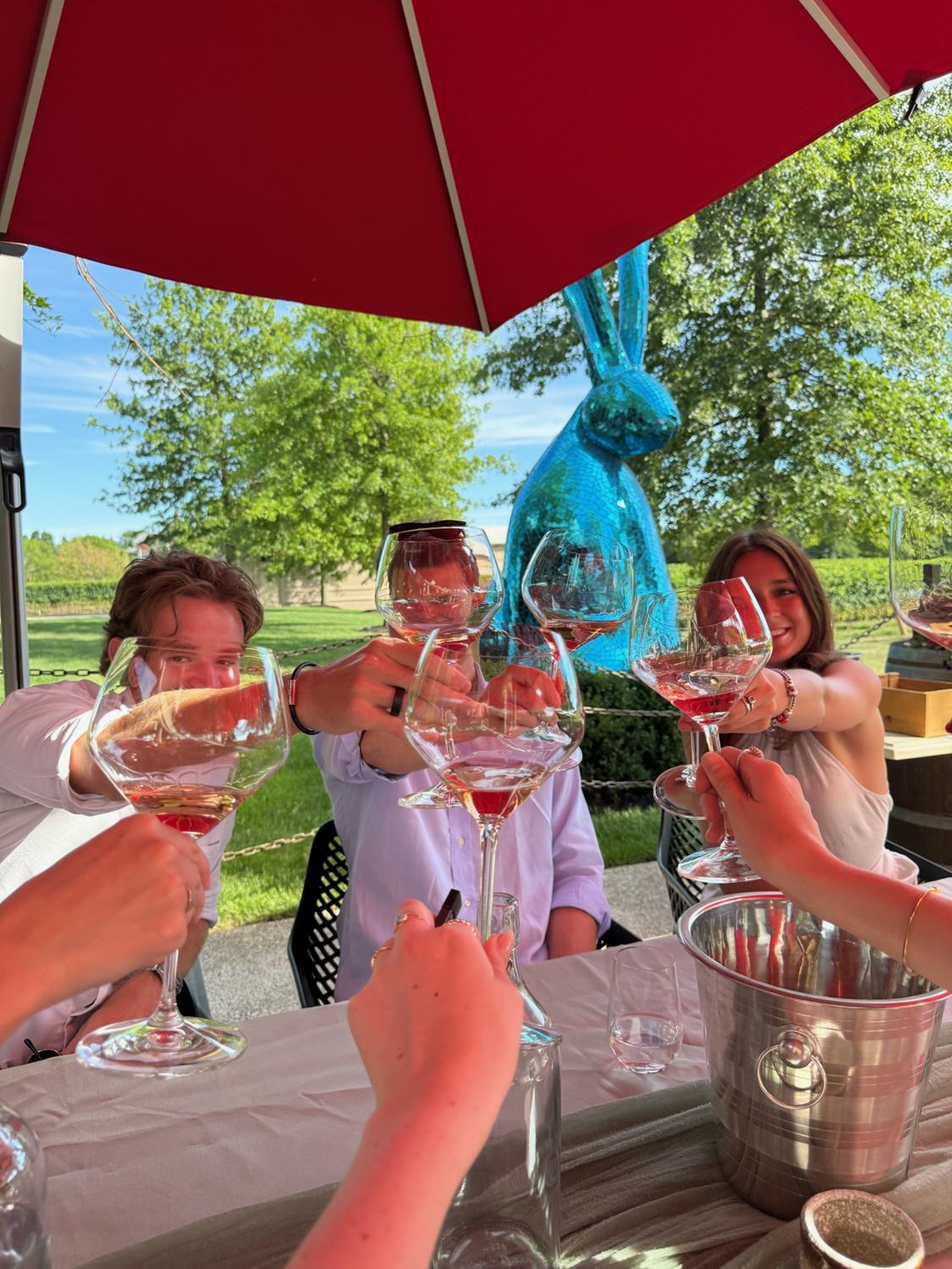 Glasses of rosé raised in a toast under a red umbrella
