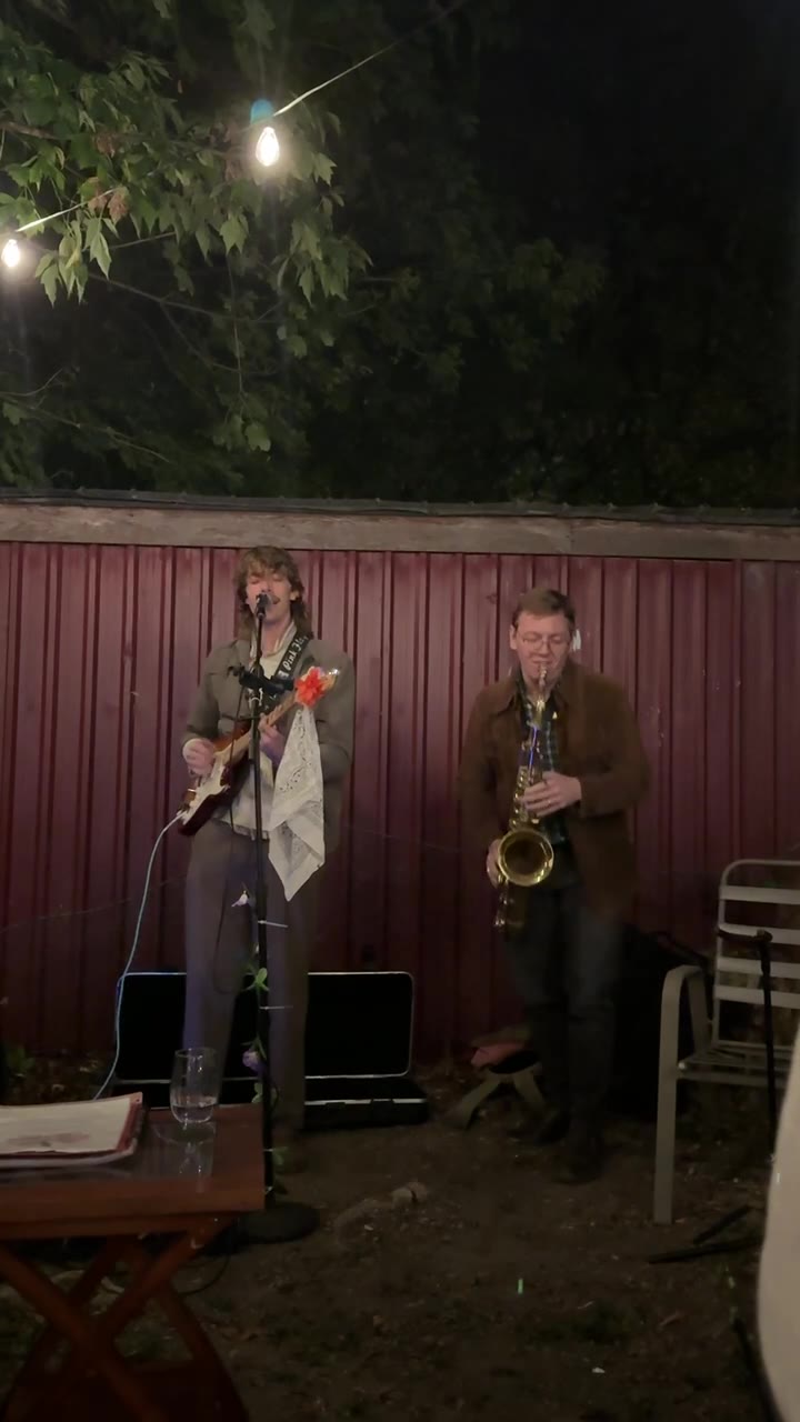 A guitarist and a saxophonist playing under string lights